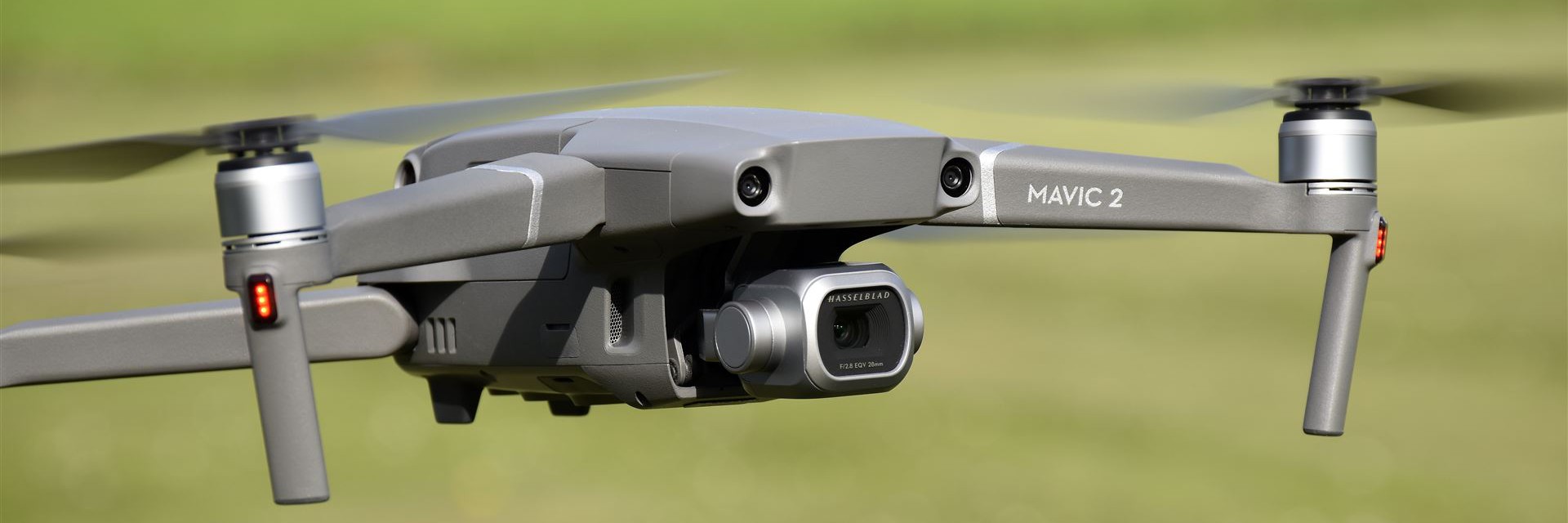 Ein grauer DJI Mavic 2 Quadcopter fliegt über einem unscharfen grünen Feld.