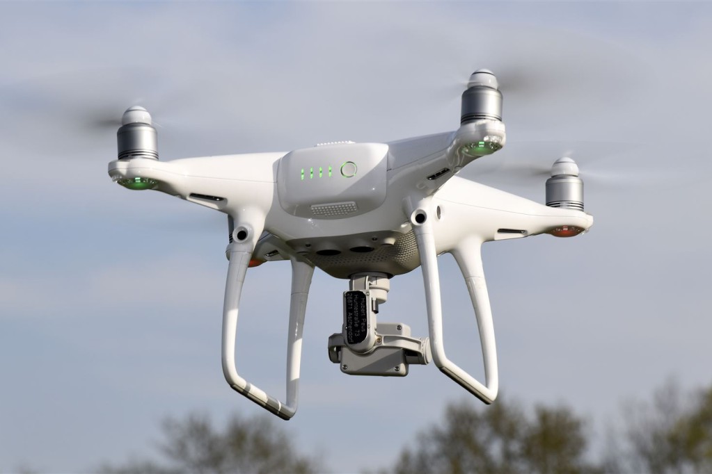 Ein moderner, weißer Quadrocopter fliegt stabil in der Luft vor einem bewölkten Himmel.